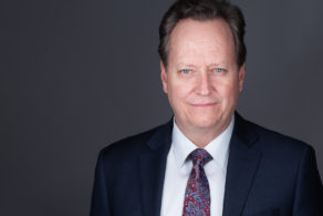 professional headshot of a middle aged man in a suit jacket white shirt and tie on a grey background in ottawa