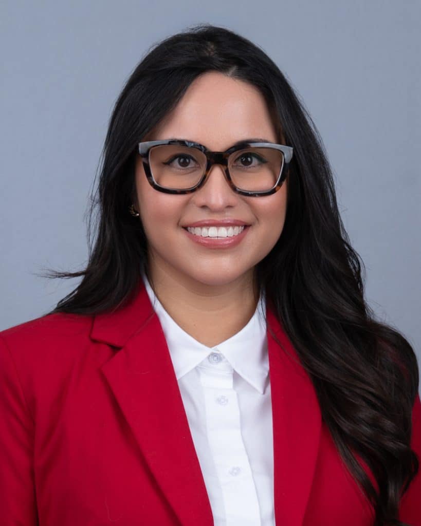 headshot of young woman in red jacket, white top and thick stylish glasses