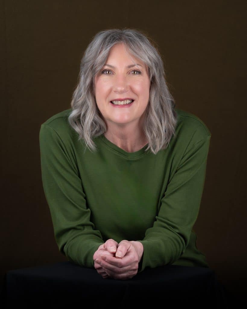 Casual headshot of Ottawa woman with grey hair in green top, darker green background
