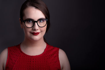 Young woman wearing glasses in a red dress on black background posing for her headshot ottawa